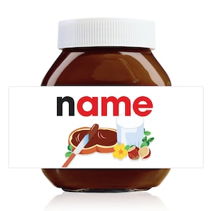 Pode incluir: Um frasco de vidro de pasta de chocolate e avelã com tampa branca e um rótulo que diz "name" em letras vermelhas e pretas. O rótulo também apresenta uma ilustração de desenho animado de uma faca espalhando a pasta em uma fatia de pão, um copo de leite e avelãs.