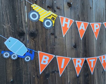 May include: Orange and white construction vehicle themed banner with the words "Happy Birthday" in white letters. The banner is strung on a wooden fence.