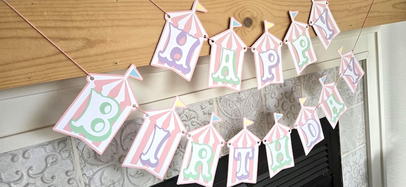 May include: A pink and white striped circus tent banner with the words "Happy Birthday" in pastel colors.