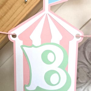May include: Pink and white striped tent banner with a green letter B inside. The tent has a blue flag on top.