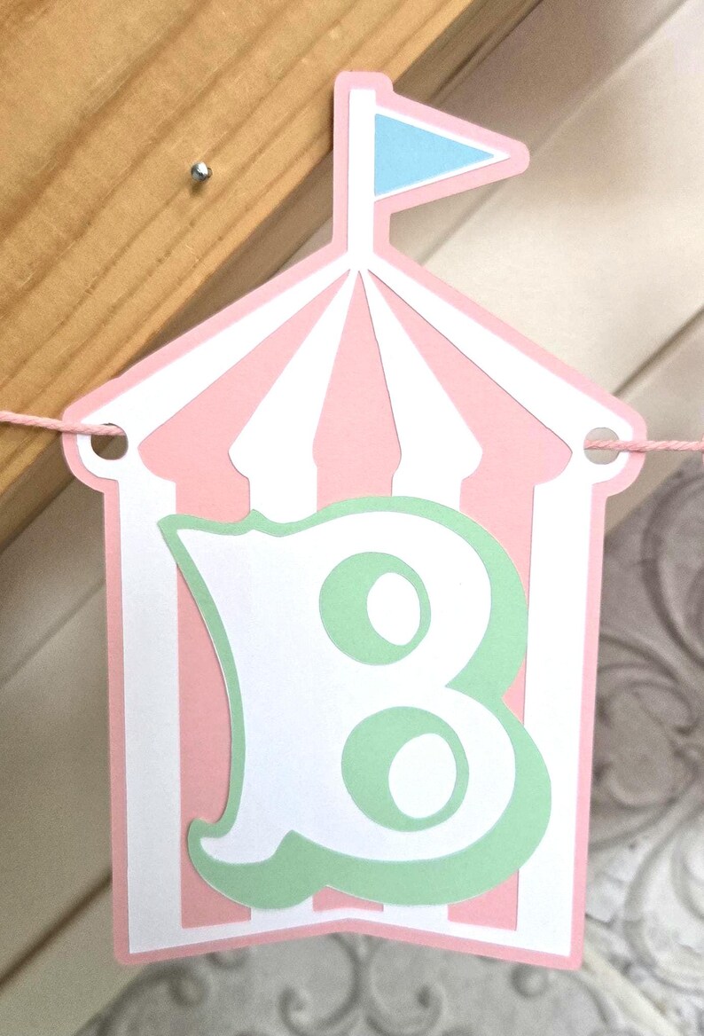 May include: Pink and white striped tent banner with a green letter B inside. The tent has a blue flag on top.