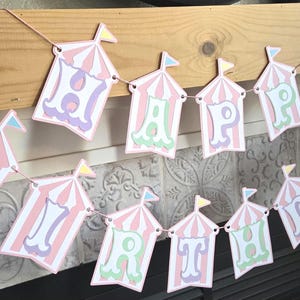 May include: A pink and white circus tent banner with the words "Happy Birthday" in pastel colors.