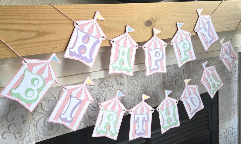 May include: A pink and white circus tent banner with the words "Happy Birthday" in pastel colors.