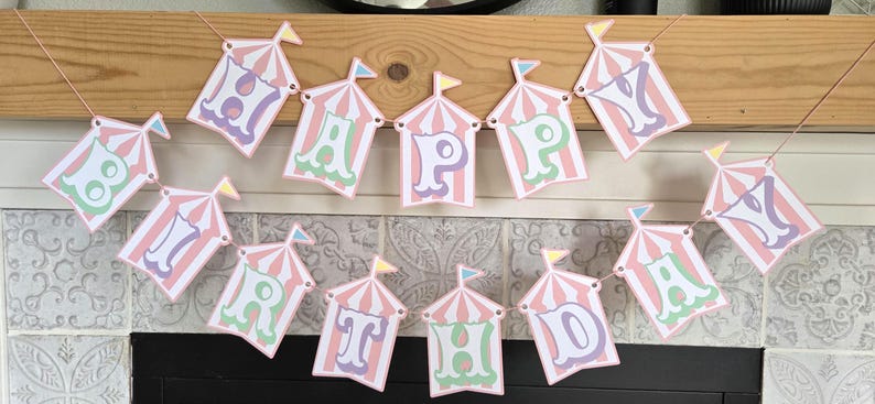 May include: A pink and white circus tent themed banner with the words "Happy Birthday" in pastel colors.