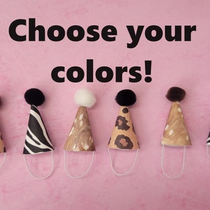 May include: Six miniature party hats with different animal print designs. The hats are brown, black, and white with a pom-pom on top. The text "Choose your colors!" is at the top of the image.