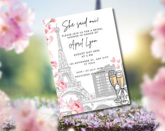 May include: Bridal shower invitation with the text "She said oui!" featuring a gray Eiffel Tower illustration, pink floral accents, and champagne glasses. The invitation includes event details for April Lynn on August 21st, 2025.