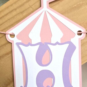 May include: Pink and white circus tent banner with a purple letter H. The banner is strung with white twine.