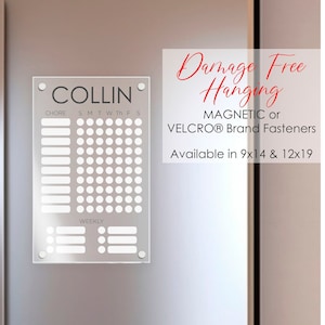 May include: A white dry-erase chore chart with the word "COLLIN" at the top. The chart is divided into days of the week and has spaces for writing chores. The chart is hanging on a stainless steel refrigerator. The text "Damage Free Hanging" is written in red cursive. The text "MAGNETIC or VELCRO® Brand Fasteners" is written in black. The text "Available in 9x14 & 12x19" is written in black.