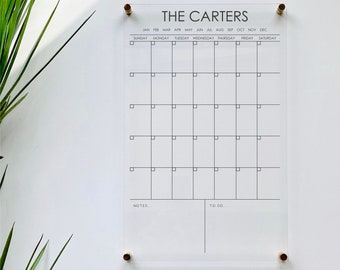 May include: A clear acrylic calendar with the text "THE CARTERS" at the top. The calendar has a grid for each month of the year, with spaces for each day. There are also sections for notes and to-do items.