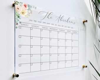 May include: A clear acrylic monthly calendar with a floral design and the text "The Abrahams". The calendar has a grid with boxes for each day of the month, labeled with the days of the week and months of the year. There is a small section labeled "notes".