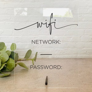 May include: A clear acrylic sign with the word "wifi" written in cursive. The sign also has the words "NETWORK" and "PASSWORD" with blank lines underneath for writing in the network name and password.