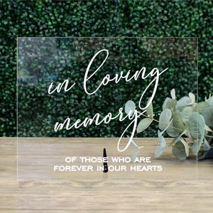 May include: A clear acrylic sign with the text "In loving memory... of those who are forever in our hearts".