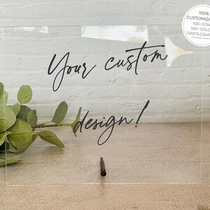 May include: A clear acrylic sign with the text "Your custom design!" written in black ink. The sign is 100% customizable with 100+ fonts, 100+ colors, and 1,000's of graphics.