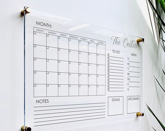 May include: A clear acrylic dry erase calendar with a monthly grid, to-do list, menu planner, notes section, goals section, and upcoming events section. The calendar is labeled "MONTH:" and has the days of the week listed across the top. The calendar also has the text "The Carters" at the top right corner.
