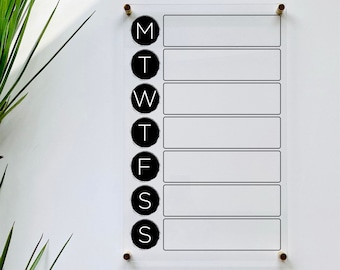 May include: A clear acrylic weekly planner with black circles and white letters for each day of the week: M, T, W, T, F, S, S.