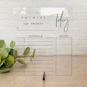 May include: A clear acrylic dry erase board with a daily planner layout. The board has sections for "Top Priority", "Schedule", and "Notes". The text "Today" is written in cursive at the top of the board.