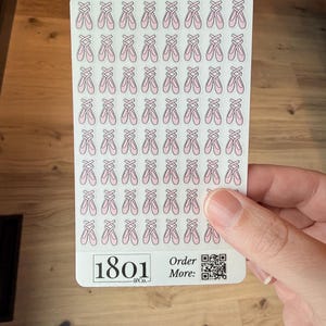 May include: A sheet of stickers featuring rows of pink ballet slippers. The stickers are held by a hand. The bottom of the sticker sheet has the text "1801 & Co." and "Order More:" with a QR code.