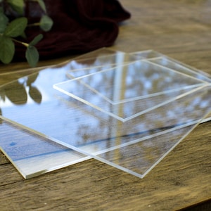 May include: Three clear acrylic sheets of different sizes stacked on top of each other on a wooden surface.