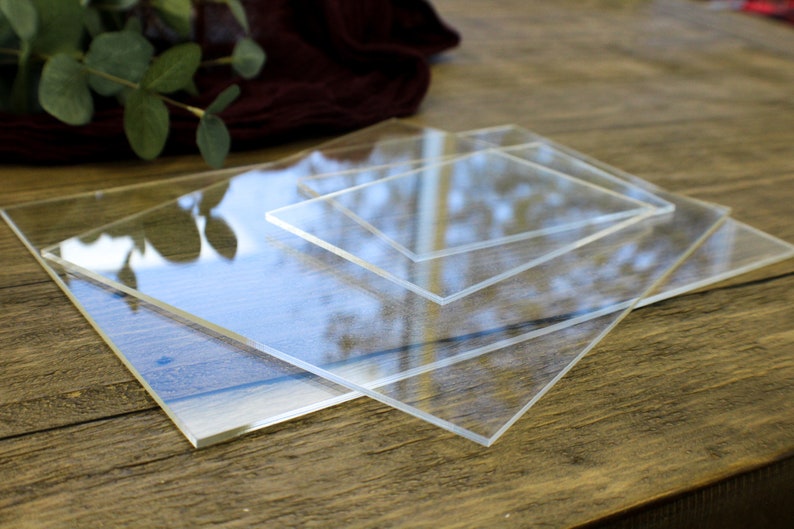 May include: Three clear acrylic sheets of different sizes stacked on top of each other on a wooden surface.