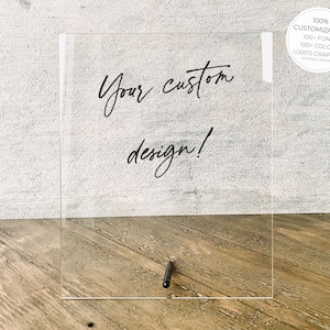 May include: A clear acrylic sign with the text "Your custom design!" written in black cursive. The sign is 100% customizable with 100+ fonts, 100+ colors, and 1,000's of graphics.