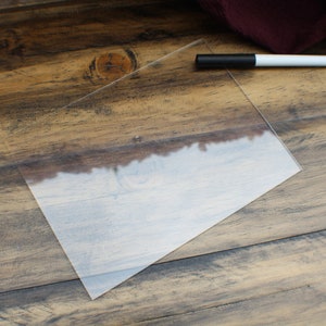 May include: A clear acrylic sheet on a wooden surface with a white dry-erase marker.