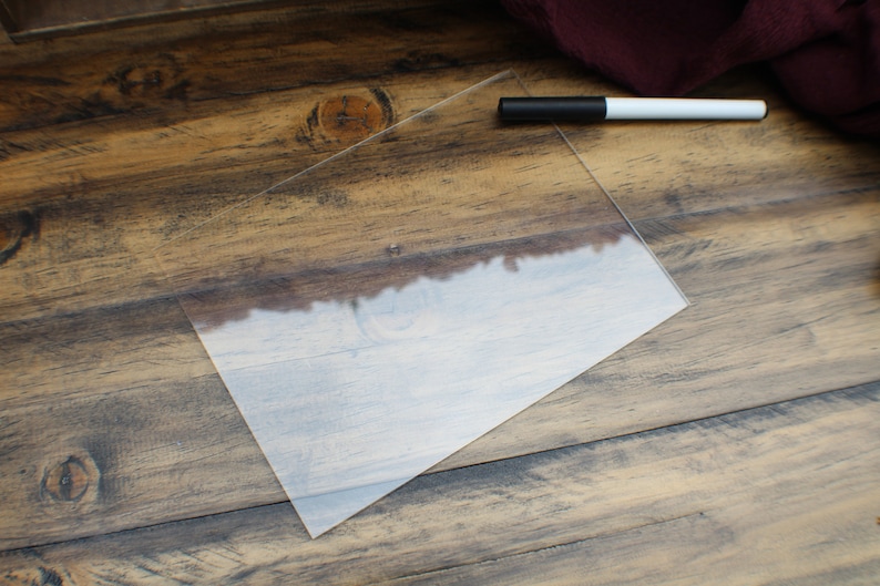 May include: A clear acrylic sheet on a wooden surface with a white dry-erase marker.