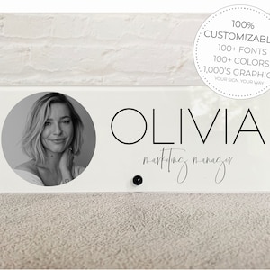May include: A white acrylic desk sign with a black and white photo of a woman in a circle. The text "OLIVIA marketing manager" is printed in black on the sign.