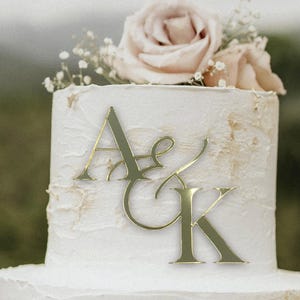 May include: A white wedding cake with gold letters that say "A & K" on top.
