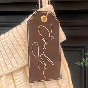 May include: A brown leather gift tag with a gold metal eyelet and the name "Audrey" written in cursive script.