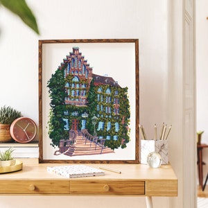 May include: A framed illustration of a brick building with a steep roof covered in green ivy. The building has a set of stairs leading up to the entrance. The illustration is in a brown frame and is hanging on a white wall.