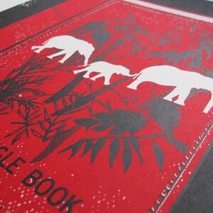 May include: Red and black illustration of elephants walking through a jungle with the text "The Jungle Book" printed on the bottom left corner.
