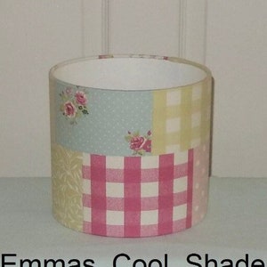 May include: A pink, yellow and blue patchwork lampshade with a floral pattern. The lampshade is cylindrical and has a white interior. The text "Fryetts Vintage Patchwork Pink" is printed below the lampshade.