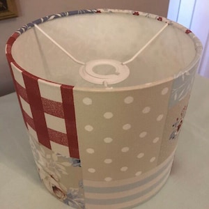 May include: A white lampshade with a patchwork design featuring red and white gingham, beige with white polka dots, and blue and white stripes.