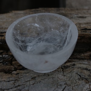 Puede incluir: Un cuenco de cristal de cuarzo transparente con una superficie lisa y pulida. El cuenco está hecho de cuarzo natural y tiene una forma orgánica única.