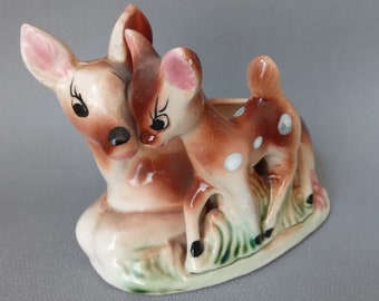 May include: A ceramic planter shaped like two deer, one larger than the other. The deer are brown with white spots and have pink noses. The planter is a light brown color with green accents.