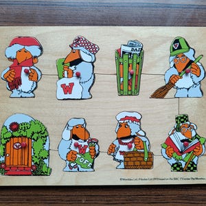 Puede incluir: Rompecabezas de madera vintage con ocho personajes de dibujos animados con picos naranjas y varios accesorios. Los personajes están sobre un fondo marrón claro. El rompecabezas incluye una puerta, un cubo de basura y personajes que sostienen objetos. El texto "TOFF" es visible.