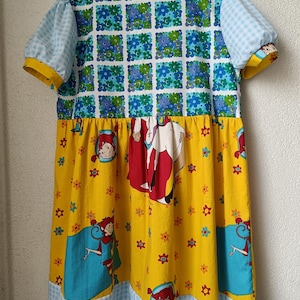 以下が含まれることがあります： パッチワークデザインが特徴的なカラフルなドレス。上部は青と白の花柄で、袖は黄色のトリムが付いた水色のギンガムチェック。スカートは黄色で、漫画のキャラクターのイラストと青と白のギンガムチェックの裾が付いています。