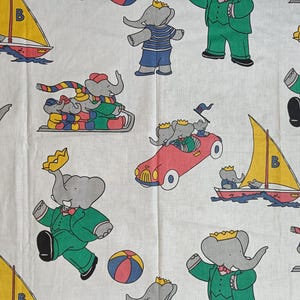 May include: White fabric with a repeating pattern of cartoon elephants wearing crowns and outfits. The elephants are depicted in various activities, including sailing, driving a car, and playing with a ball. The color palette includes green, red, yellow, and blue.