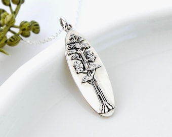 May include: A silver pendant necklace featuring an oval-shaped pendant with a detailed tree design. The tree is depicted with a textured trunk and layered foliage. The pendant hangs from a delicate silver chain, creating an elegant accessory.