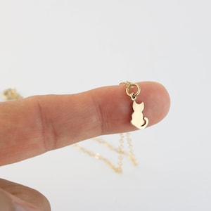 以下が含まれることがあります： 小さな猫のペンダントが付いた繊細なゴールドカラーのネックレス。ペンダントは座っている猫のシルエットです。ネックレスは細いゴールドチェーンで、普段使いに最適です。