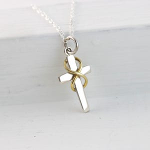 May include: Silver cross pendant with a gold-colored infinity symbol wrapped around it. The cross is suspended from a delicate silver chain. The pendant is a religious symbol.