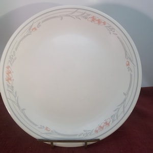 Könnte beinhalten: Ein weißer Keramik-Dinnerteller mit einem grauen und pfirsichfarbenen Blumendesign am Rand.