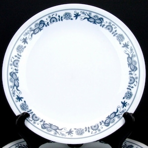 Peut inclure: Une assiette plate en céramique blanche avec une bordure florale bleue. La bordure présente un motif répétitif de fleurs stylisées, de feuilles et de papillons.