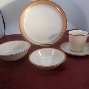 May include: A set of brown and white ceramic dinnerware, including a large dinner plate, a smaller plate, a bowl, and a cup and saucer.