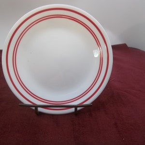 Può includere: Piatto in ceramica bianca con due bande rosse intorno al bordo.