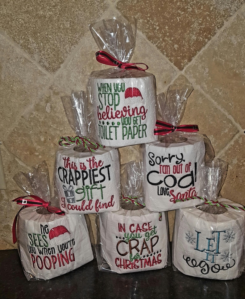May include: Five rolls of toilet paper wrapped in clear plastic with red and green ribbon. Each roll has a different embroidered Christmas-themed message. The messages are: "When you stop believing you get toilet paper", "This is the crappiest gift I could find", "Sorry ran out of coal Love Santa", "In case you get crap for Christmas", and "Let it go".
