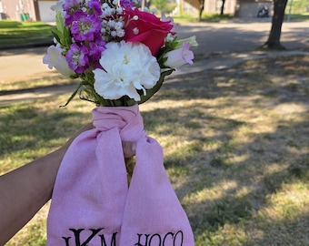 May include: A bouquet of fresh flowers featuring a vibrant mix of pink roses, white carnations, and purple stock. The bouquet is tied with a pink fabric that has the text "IKM HOCO 2025" embroidered in black.