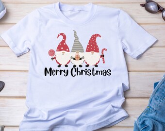 Könnte beinhalten: Ein hellblaues T-Shirt mit einem Motiv von drei Gnomen, die rote Mützen tragen und einen Zuckerstock, ein Geschenk und einen Lutscher halten. Der Text "Frohe Weihnachten" ist unter den Gnomen gedruckt.