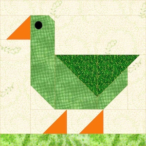 May include: A green goose with an orange beak and legs, made from fabric scraps. The goose is standing on a green and white background.
