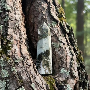 May include: A polished stone tower with a hexagonal base and a pointed top, featuring a marbled pattern of white, cream, and deep forest green colors. The object has a smooth, reflective surface with visible natural mineral inclusions throughout.